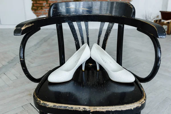Sapatos de casamento brancos em uma cadeira preta . Imagens Royalty-Free