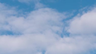 Mavi gökyüzünde beyaz bulutlar (yatay hareket). Pofuduk beyaz bulutlar mavi gökyüzü arka planında soldan sağa uçar. Zaman aşımı.