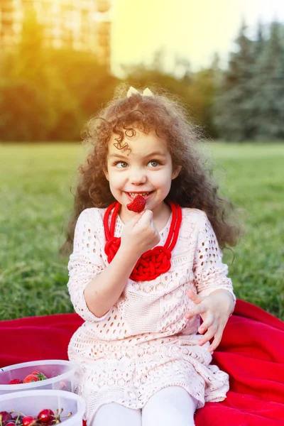 在夏天 一个晴朗的阳光明媚的一天在公园里一个小滑稽的卷发女孩吃大红色草莓 野餐概念 — 图库照片