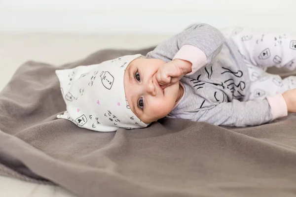 Lindo bebé sobre fondo blanco.Primer plano de la cabeza de una niña caucásica, bebé de seis meses en una ropa gris y sombrero blanco mirando a la cámara — Foto de Stock