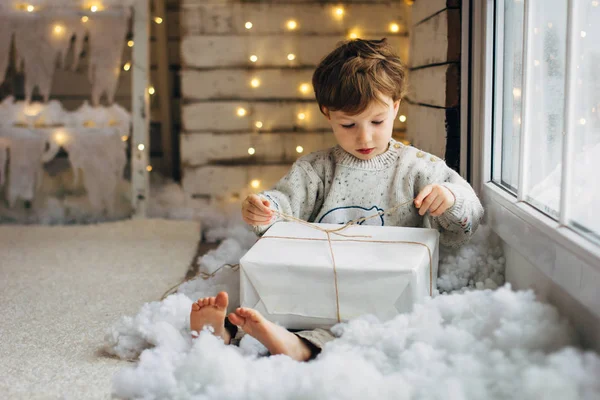 Rapaz de cabelo encaracolado a abrir o seu presente de Natal. Ano novo luzes fundo — Fotografia de Stock