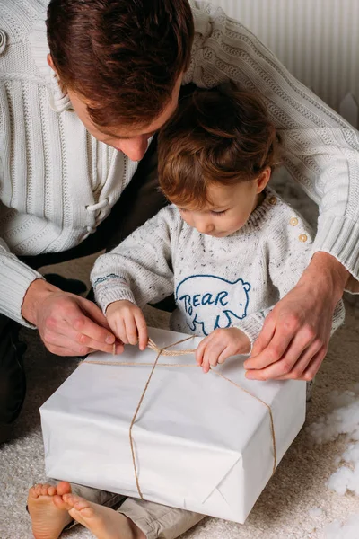 Pai e filho felizes segurando presentes de Natal na sala de estar. Árvore de crismas e fundo de madeira — Fotografia de Stock