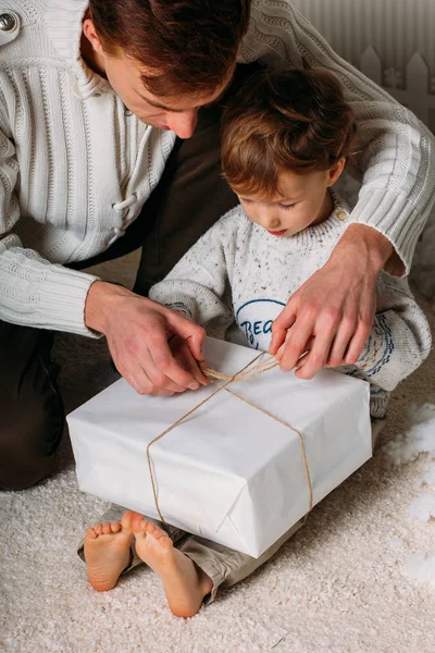 Pai e filho felizes segurando presentes de Natal na sala de estar. Árvore de crismas e fundo de madeira — Fotografia de Stock