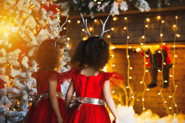 İki küçük kız yakınındaki güzel Noel ağacı Noel şömine bakarak. İkizler Santa şömine görünümlü kırmızı elbiseler.