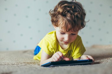 Küçük yakışıklı bir yeşil T-shirt bir tablet üzerinde oyun ve çizgi film izlemek