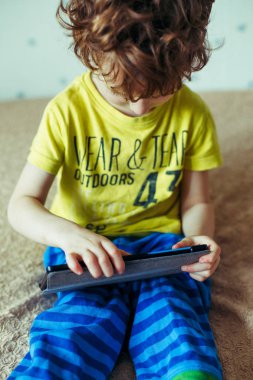 Küçük yakışıklı bir yeşil T-shirt bir tablet üzerinde oyun ve çizgi film izlemek