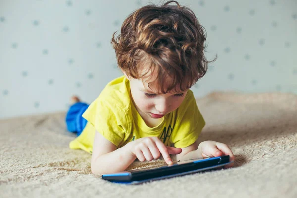 Küçük yakışıklı bir yeşil T-shirt bir tablet üzerinde oyun ve çizgi film izlemek