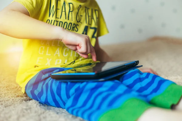 Kleine schattige jongen in een groen T-shirt spelen op een tablet en kijken cartoons. verslaving concept — Stockfoto