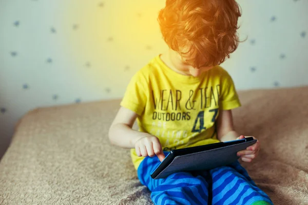 Kleiner süßer Junge in grünem T-Shirt, der auf einem Tablet Spiele spielt und sich Cartoons ansieht. Suchtkonzept — Stockfoto