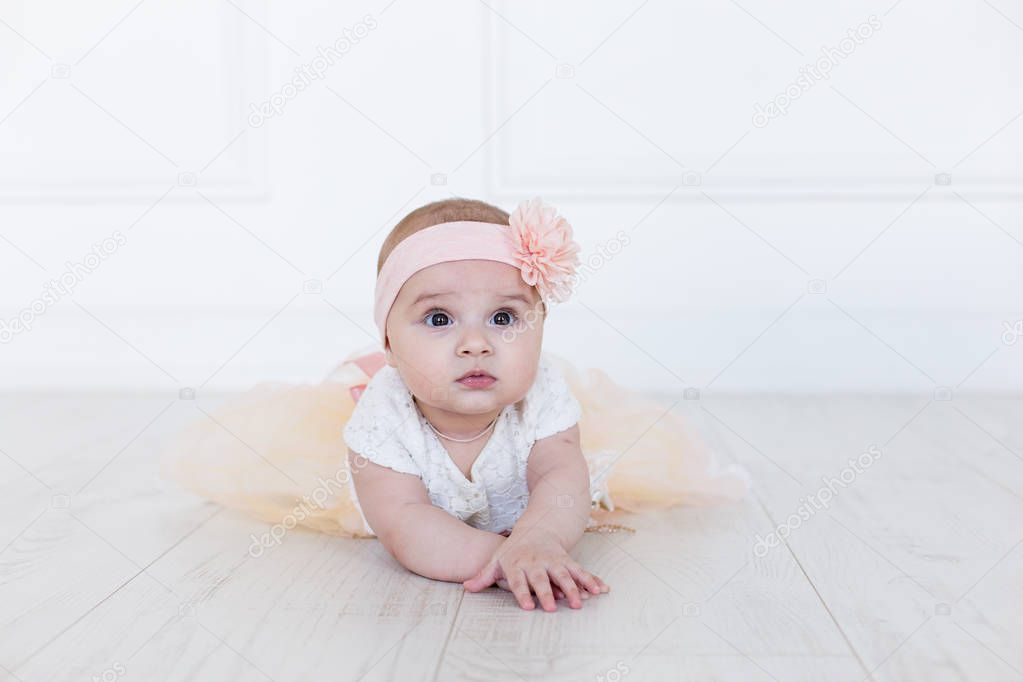 A baby girl is crawling along the floor with an inquisitive and wondering look on her face. Horizontal shot.