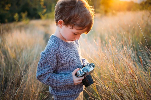 秋の草背景に古いレトロなビンテージ カメラでかわいい幼児少年 写真で遊んで巻き毛の子 — ストック写真