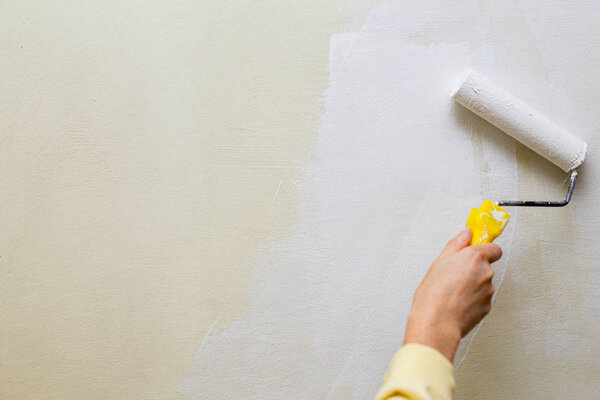 Photo of a female painting a wall with a roller and white paint. Horizontal photo. Copy space