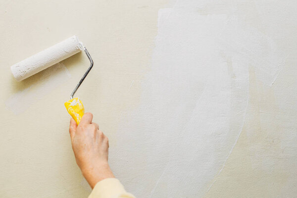 Photo of a female painting a wall with a roller and white paint. Horizontal photo. Copy space
