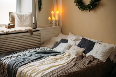 Parlak rahat modern yatak odası tatil dekorasyonu ile. Yatak yatak takımları küme ve Örgü yastık, ahşap raf, güzel Noel ağacı çelenk duvarın ve mum ışığı gri.