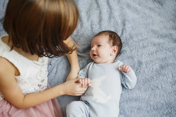 Cute happy girl holding her newborn baby brother. Gray background. Pretty baby boy in blue clothes — Stock Photo, Image