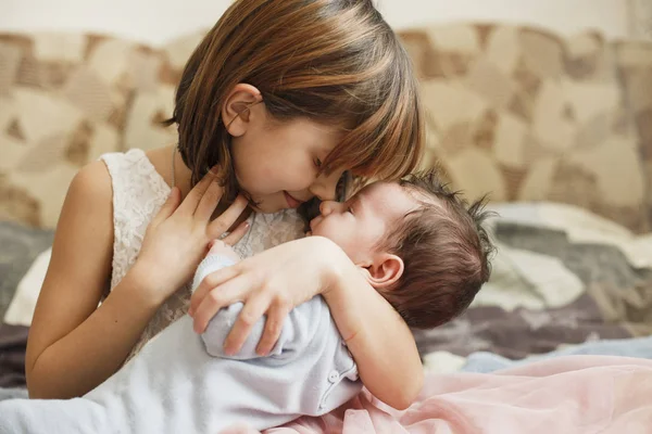 Sorellina che abbraccia suo fratello appena nato. Un bambino che incontra un nuovo fratello. Ragazza carina e neonato si rilassano in una camera da letto a casa. Famiglia con bambini a casa. Amore, fiducia e tenerezza — Foto Stock