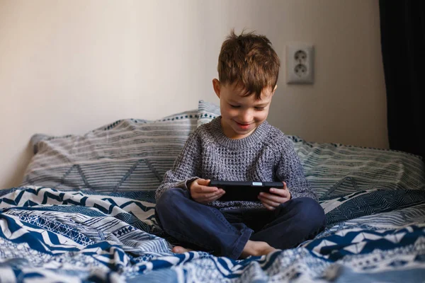 Милый малыш играет со смартфоном на кровати. Концепция интернет-зависимости — стоковое фото