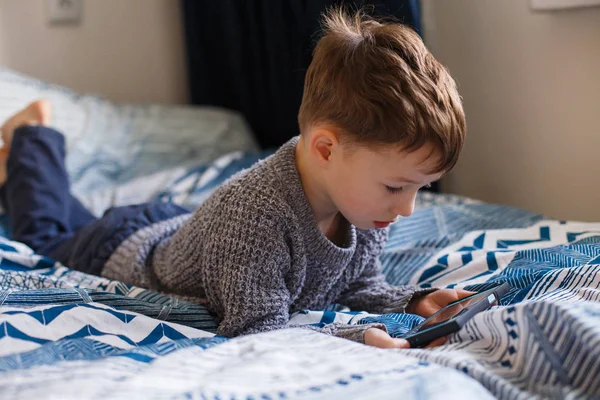 Peuter jongen ligt op zoek op de telefoon. Het concept van afhankelijkheid van gadgets — Stockfoto