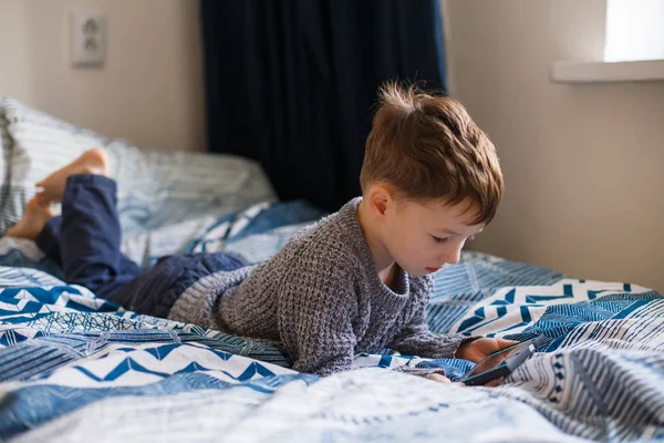 Kleinkind liegt und schaut auf das Telefon. das Konzept der Abhängigkeit von Gadgets — Stockfoto