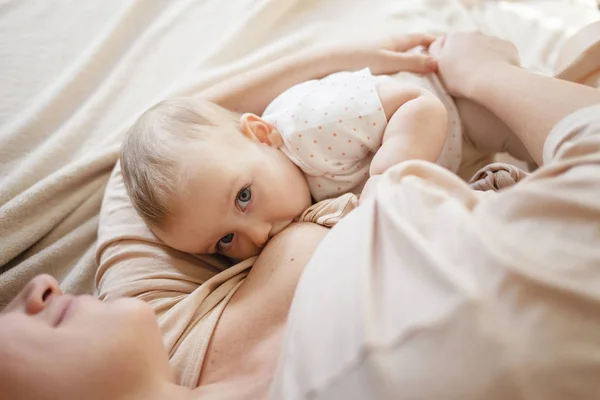 Genç breastfeeds onu kucağında tutmak ve mutluluktan gülümseyen onun bebek kız, anne. 9 ay önce çocuk