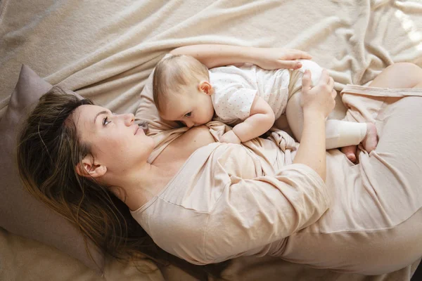 Genç breastfeeds onu kucağında tutmak ve mutluluktan gülümseyen onun bebek kız, anne. 9 ay önce çocuk
