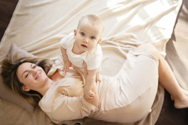 Sarılma ve kapalı yatakta yatarken oynayan anne ve bebek kız. Üstten görünüm. — Stok fotoğraf