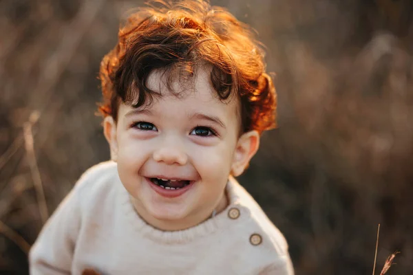 Chiudi il ritratto di un dolce bambino bambino sorridente nel parco autunnale al tramonto. Capelli ricci ragazzo — Foto Stock