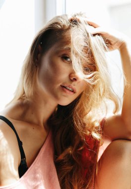 güzel sarışın kadın pencerenin yanında oturuyor ve kameraya bakıyor. Kıvırcık saçlı kız