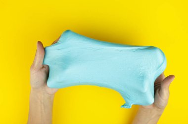 Dişi eller parlak sarı bir arka planda mavi sümükle oynuyorlar. Stres önleyici oyuncak. Rahatlama ve dinlenme.