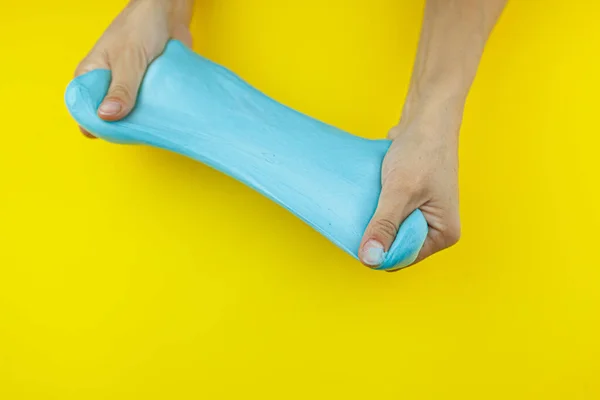 As mãos femininas estão brincando com lodo azul em um fundo amarelo brilhante. Brinquedo anti-stress. Relaxamento e repouso. — Fotografia de Stock