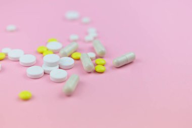 Pembe arka planda sarı ve beyaz haplar ve kapsüller. Tıbbi geçmiş.