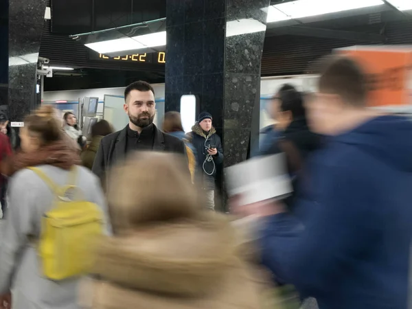 Handsome bearded man dressed in wool coat stands still in metro station within moving crowds of people — Stock Photo, Image