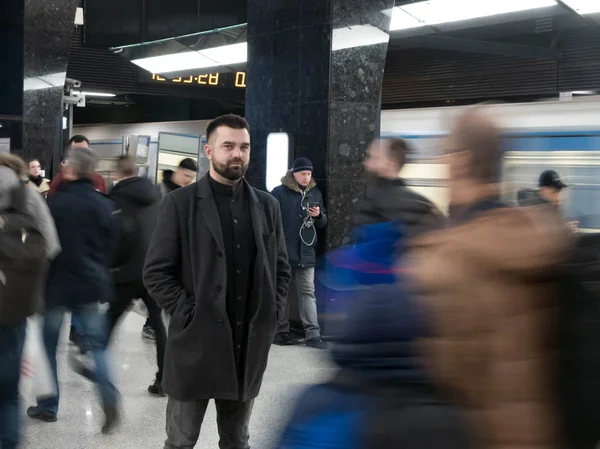 Handsome bearded man dressed in wool coat stands still in metro station within moving crowds of people — Stock Photo, Image