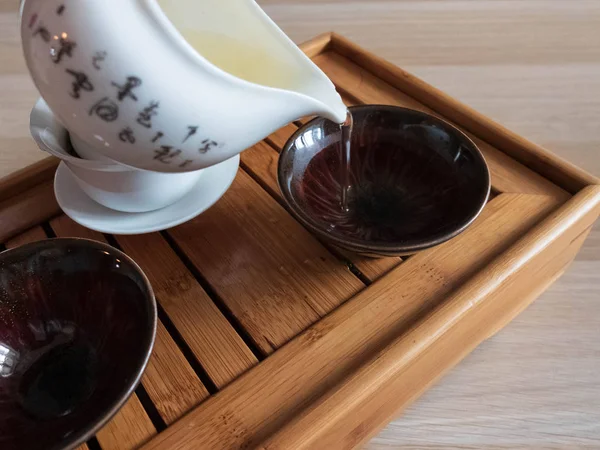 Derramando chá oolong para as tigelas de chá chawans cor de olho de fênix na bandeja de drenagem de chá . — Fotografia de Stock