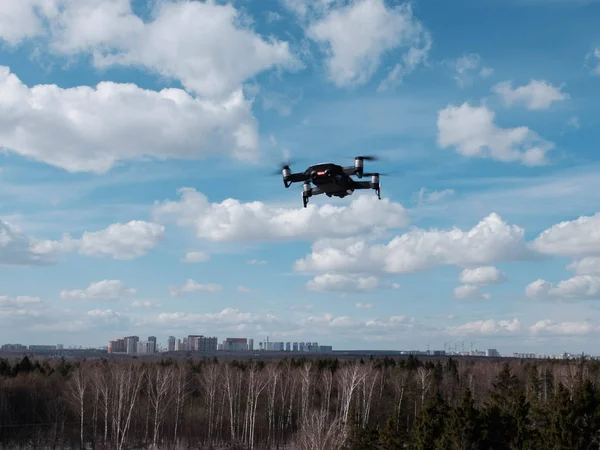 Drone in bilico nel cielo blu brillante con nuvole sopra la foresta e blocchi di città sullo sfondo — Foto Stock