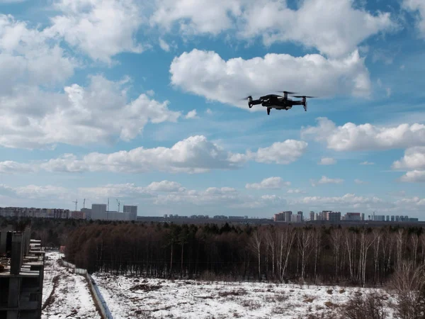 Drone in bilico nel cielo blu brillante con nuvole sopra la foresta e blocchi di città sullo sfondo — Foto Stock