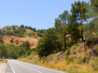 Yaz öğleden sonra yamaçlarda çam ağaçları ile Dağ yolu ve yol uyarı işareti tehlikeli eğrileri