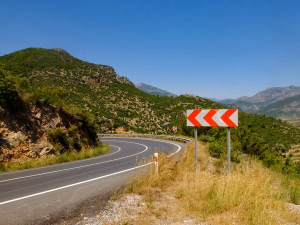 Camino de montaña en la tarde de verano y señal de advertencia de carretera curvas peligrosas — Foto de Stock