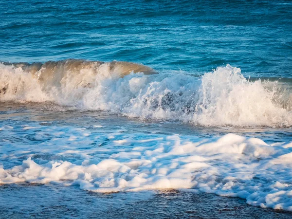 Splashing foamy waves of the sea beat on the pebble beach in the rays of the sunset — Stock Photo, Image