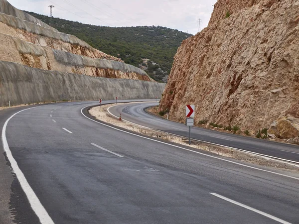 Asfaltowe krzywe drogowe pomiędzy dwoma skałami z ażurowym słupem linii energetycznych na szczycie — Zdjęcie stockowe