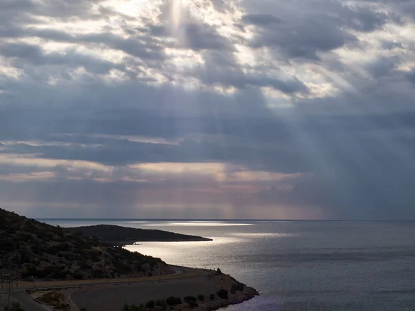 I raggi del sole sfondano le nuvole fino alla superficie del mare. Strada tortuosa al mattino — Foto Stock