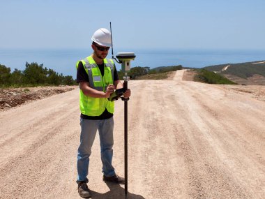 Yol inşaatı sırasında GNSS uydu alıcısıyla ölçüm yapan beyaz başlıklı jeodezi mühendisi araştırmacısı..