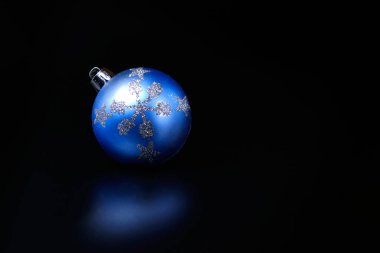 Siyah arka planda gümüş kar taneleri olan mavi Noel ağacı süsleme küresi.
