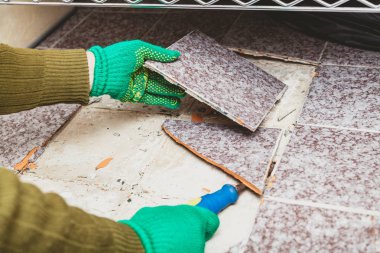 Fayansların sökülmesi. Yeşil eldivenli eller, kırık fayansı keskiyle baltalıyor.