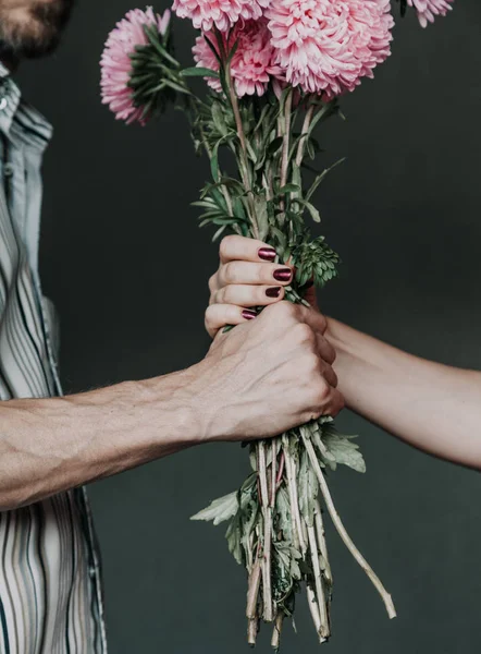 romantic moment. A man hand presents a bouquet of pink chrysanthemums to a woman hand with a beautiful manicur