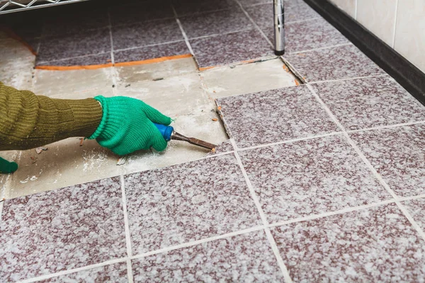 Fayansların sökülmesi. Yeşil eldivenli eller, kırık fayansı keskiyle baltalıyor.