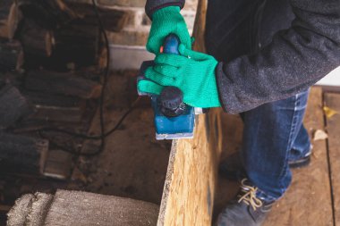 Yeşil çalışma eldiven elinde elektrikli bir planı ile ahşap plaka kenarını işlemek