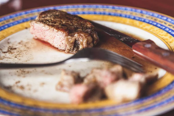 Fried beef on a plate. A sliced juicy piece of steak lies on a plate. On the right is a knife, on the left fork. Side vie