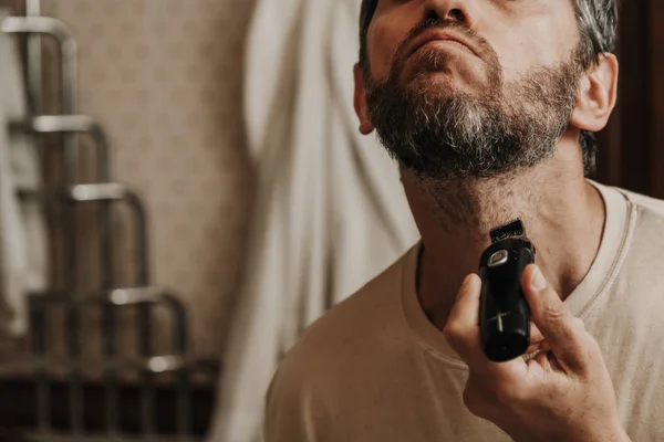 beard trimmer trimmer. The man independently cuts his gray beard with a machin