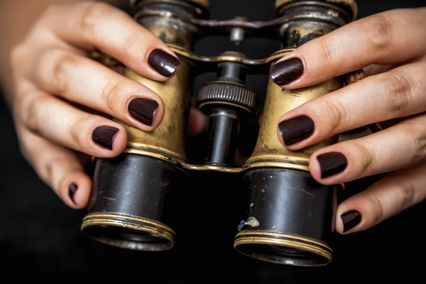 Binoculars and a woman. Beautiful female hands with manicure hold vintage metal binocular